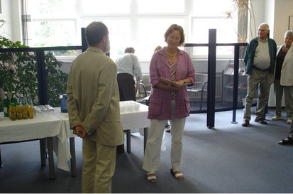 Die Abteilungsleiterin Frau Anette Drossel begrüßt Klaus Neubauer vor einer Vielzahl von kunstinteressierten Gästen.